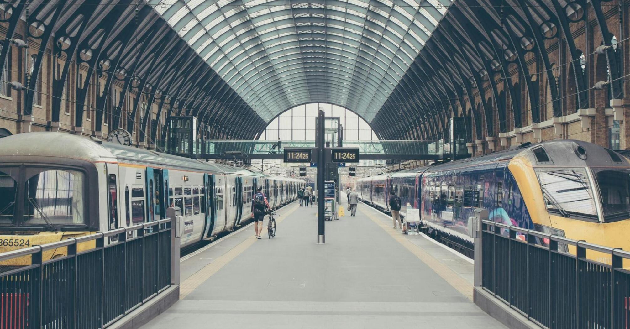 A nearly empty train station platform with two trains on either side and a few passengers walking