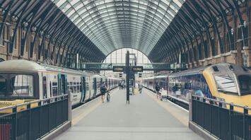 A nearly empty train station platform with two trains on either side and a few passengers walking
