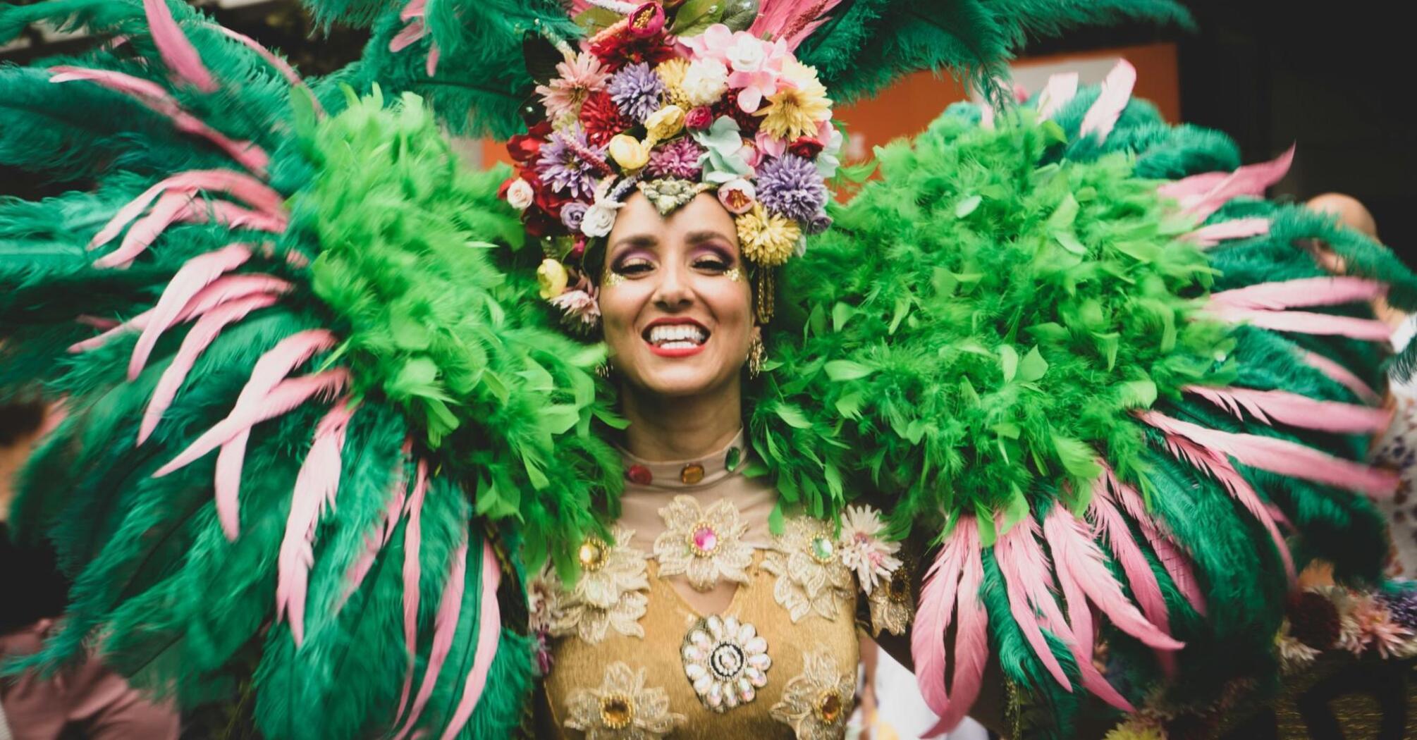 A woman in a bright carnival costume with green and pink feathers