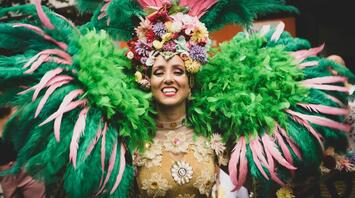 A woman in a bright carnival costume with green and pink feathers