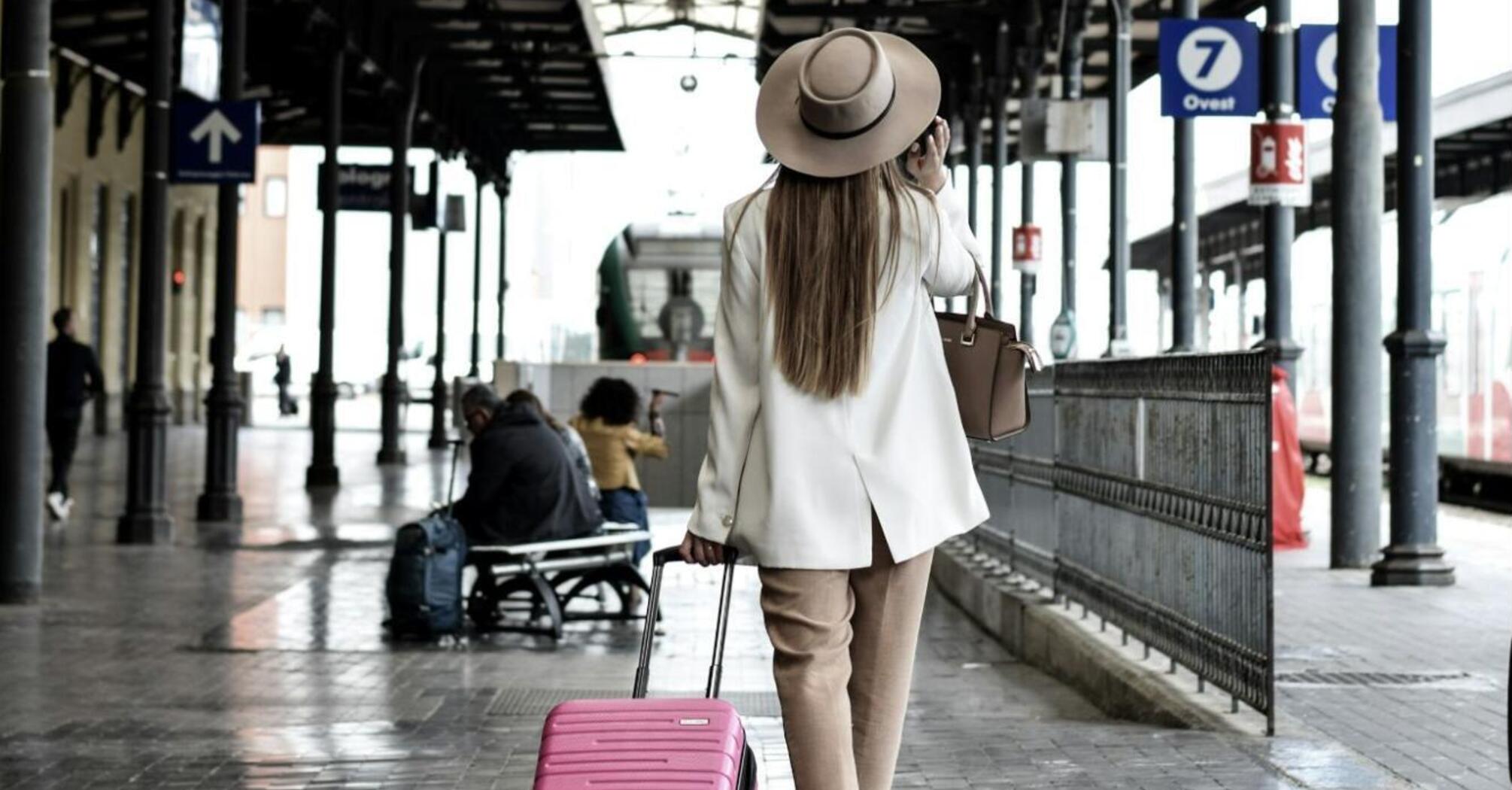 Woman with suitcase at a train station, checking the departure board
