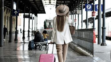 Woman with suitcase at a train station, checking the departure board