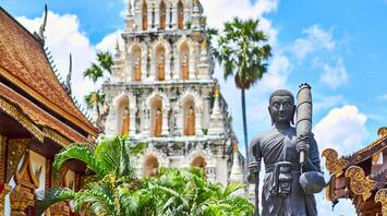 Monk statue in front of a Thai temple with a white stupa