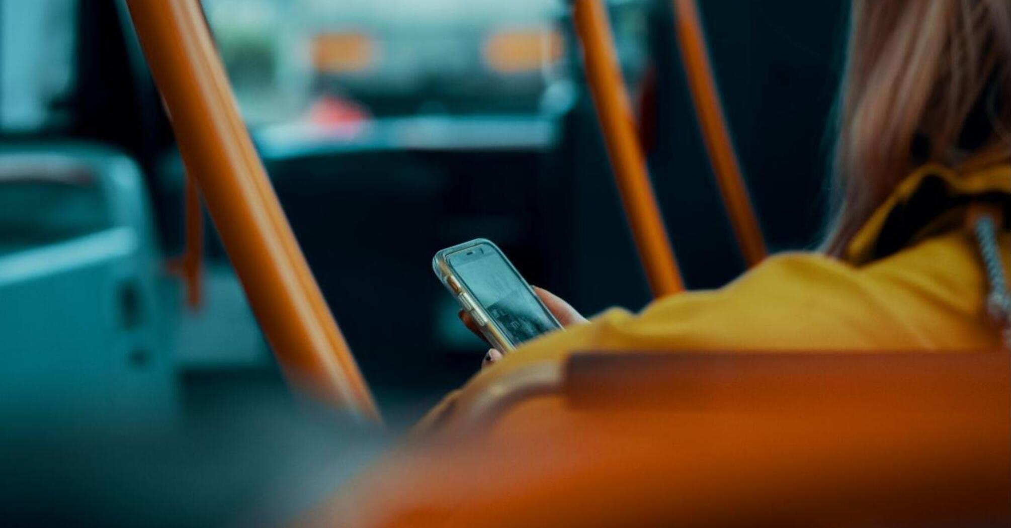 A person in a yellow jacket using a smartphone while sitting on a bus