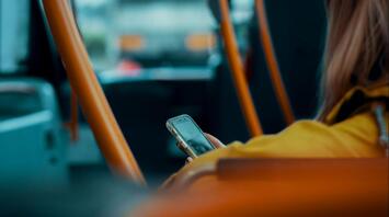A person in a yellow jacket using a smartphone while sitting on a bus