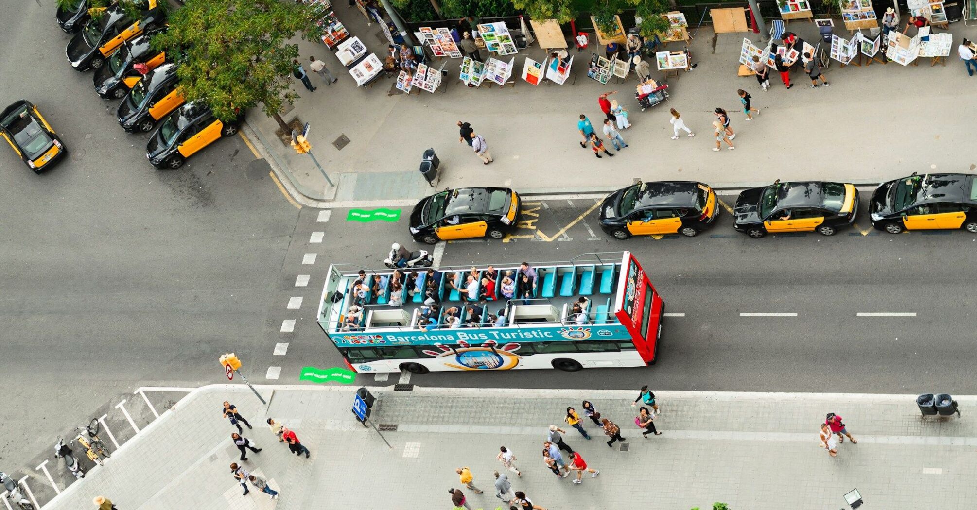 Aerial view of a busy street in Barcelona with taxis, a tourist bus, and street vendors