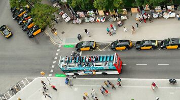 Aerial view of a busy street in Barcelona with taxis, a tourist bus, and street vendors