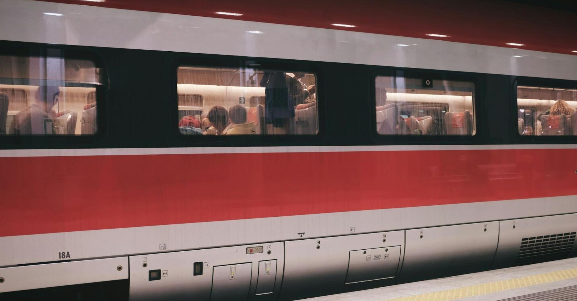 A high-speed train with passengers seated inside, visible through the windows, at a platform