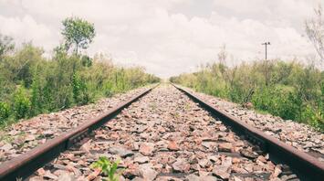 A railway track surrounded by greenery under a clear sky