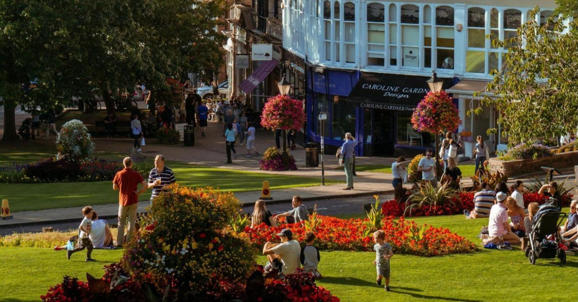 People relaxing in a sunny park surrounded by colorful flowers and historic buildings in Harrogate