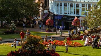 People relaxing in a sunny park surrounded by colorful flowers and historic buildings in Harrogate