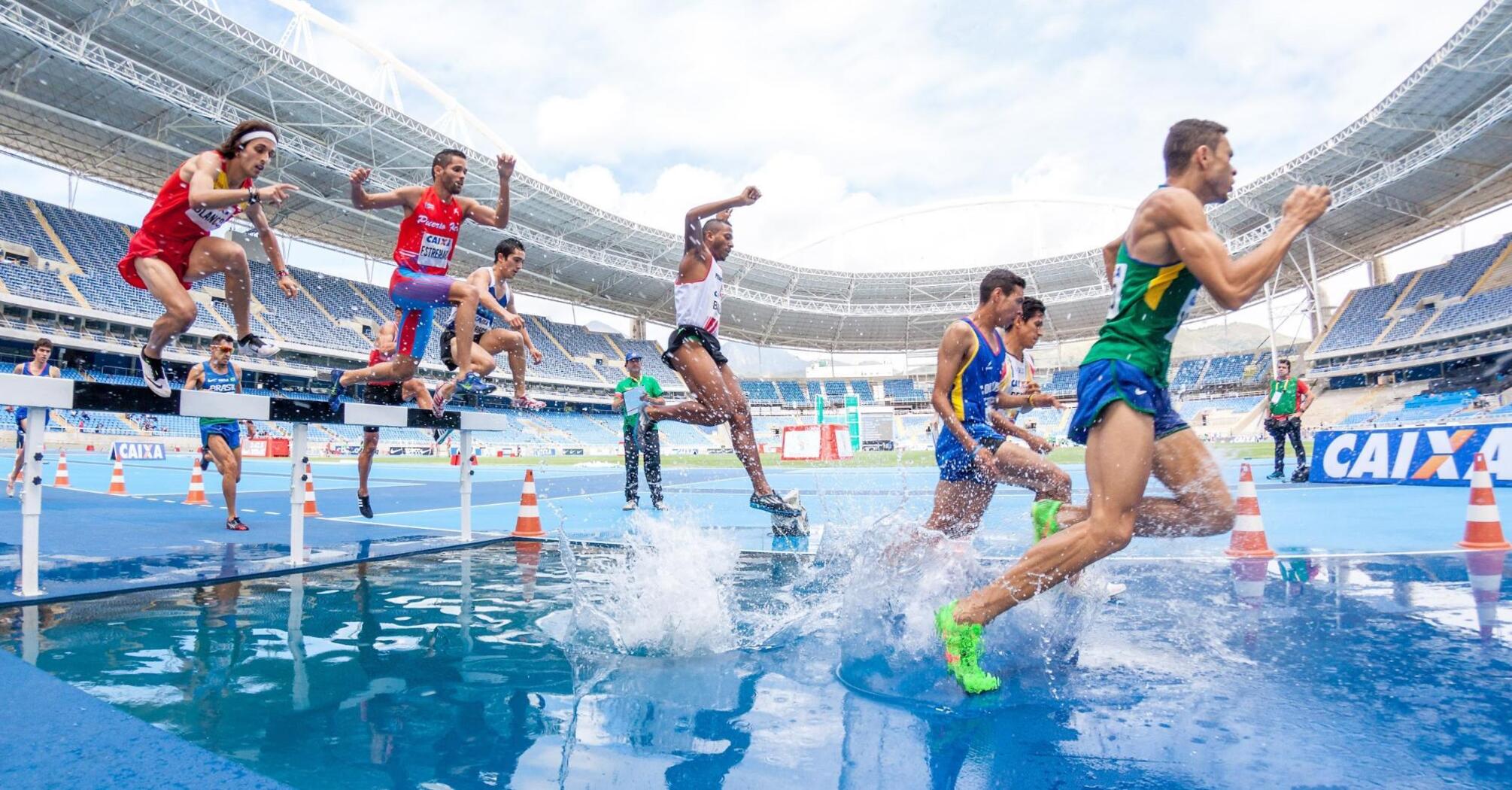 A group of runners overcoming a water obstacle during a steeplechase competition at the stadium