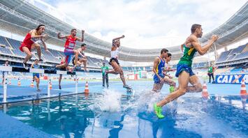 A group of runners overcoming a water obstacle during a steeplechase competition at the stadium
