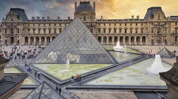View of the Louvre Museum and its glass pyramid in Paris at sunset
