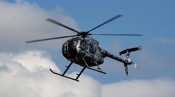 A helicopter in digital camouflage flying against a blue sky with white clouds