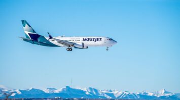WestJet aircraft in flight with mountains in the background