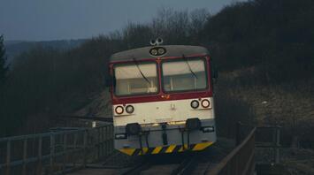 A red and white train on a railway track during dusk with a hillside in the background