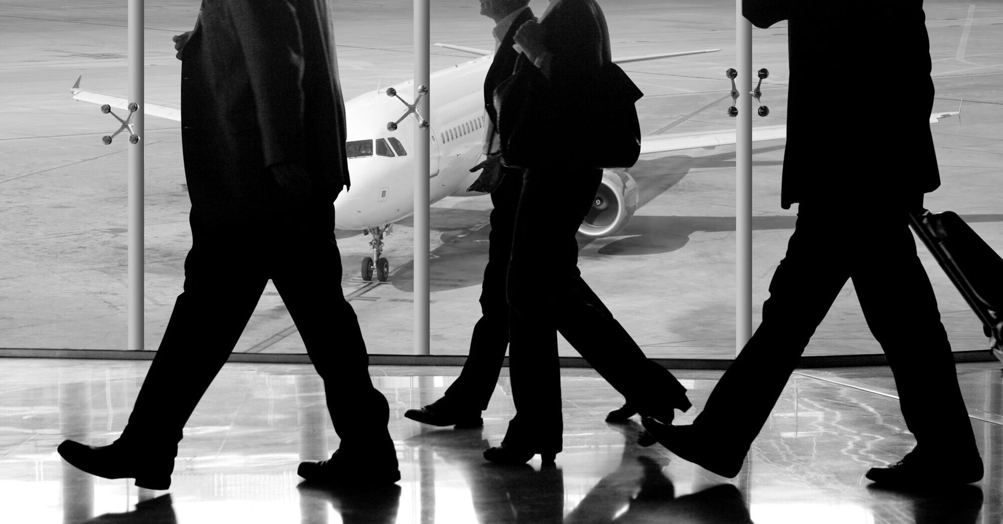 Travelers walking in an airport terminal with a plane in the background