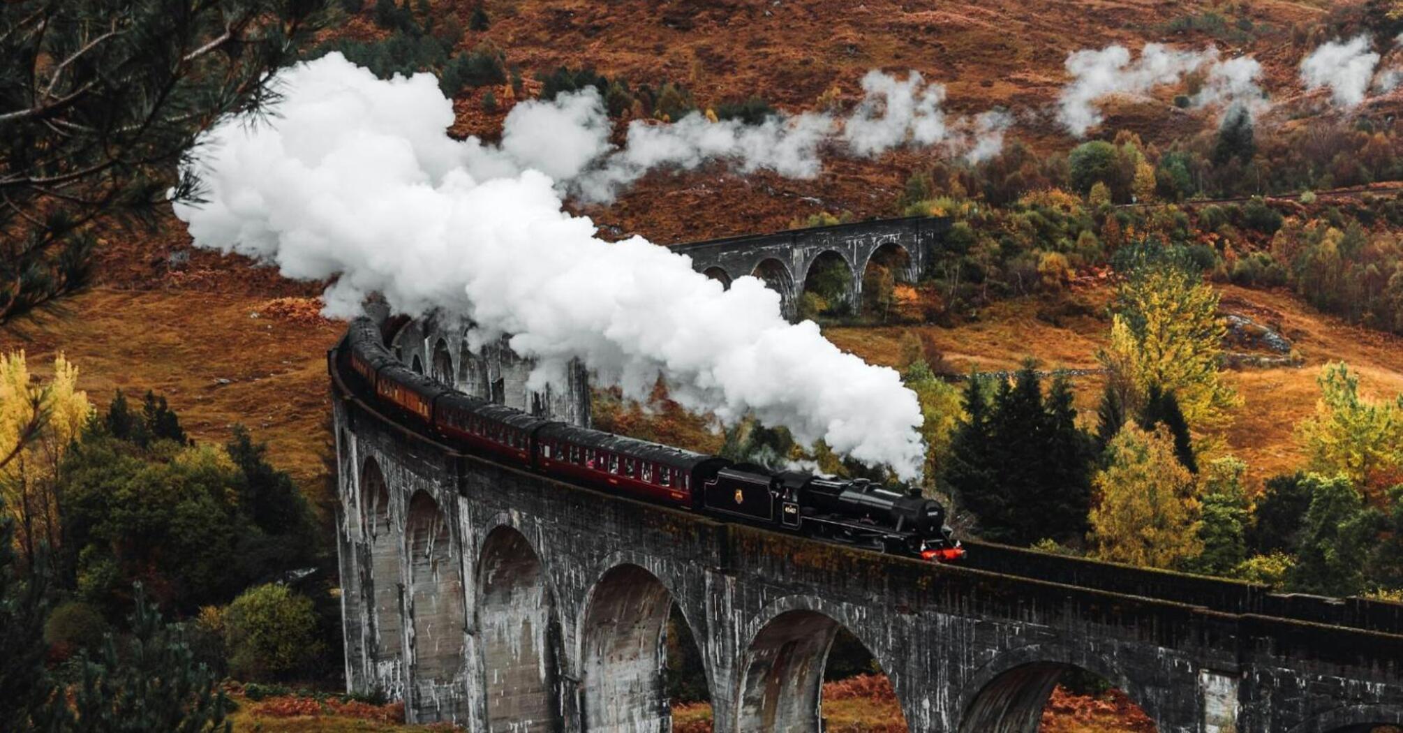 A historic steam train traveling across a picturesque viaduct