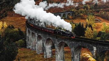 A historic steam train traveling across a picturesque viaduct