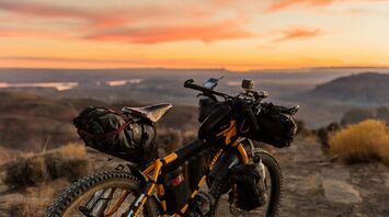 Loaded bicycle with gear at sunset overlooking a scenic landscape