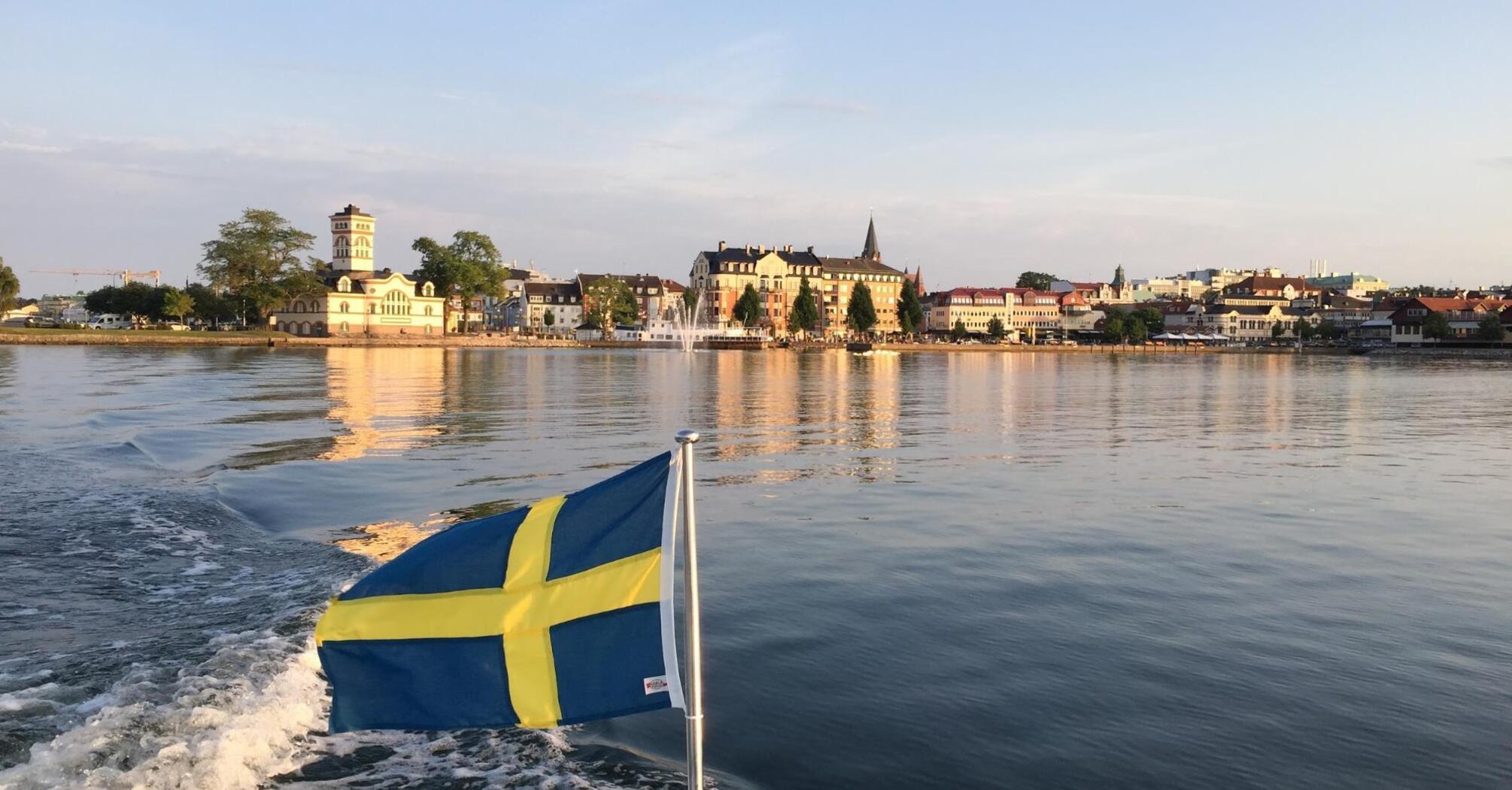 The calm waters of a Swedish lake reflect the charming architecture and the national flag