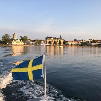The calm waters of a Swedish lake reflect the charming architecture and the national flag
