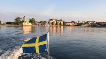 The calm waters of a Swedish lake reflect the charming architecture and the national flag