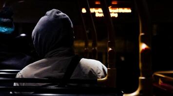 A passenger in a hoodie sits on a dimly lit bus at night