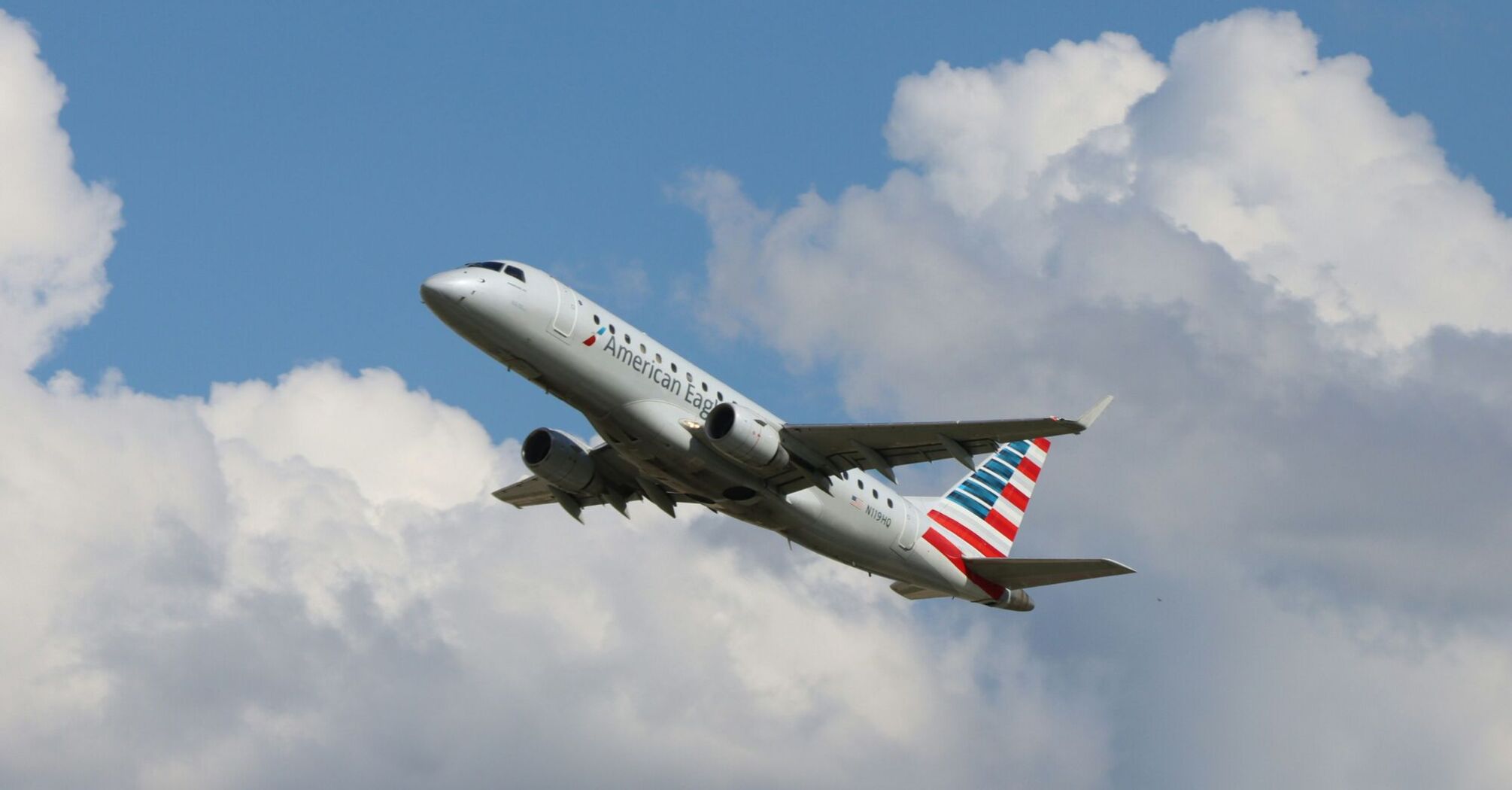 a large American Airlines passenger jet flying through a cloudy blue sky