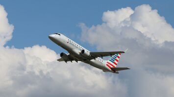 a large American Airlines passenger jet flying through a cloudy blue sky