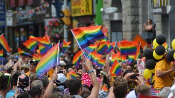 Pride festival participants joyfully wave rainbow flags on a bustling city street