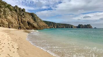 A serene beach in Penzance with clear blue water and rocky cliffs in the background