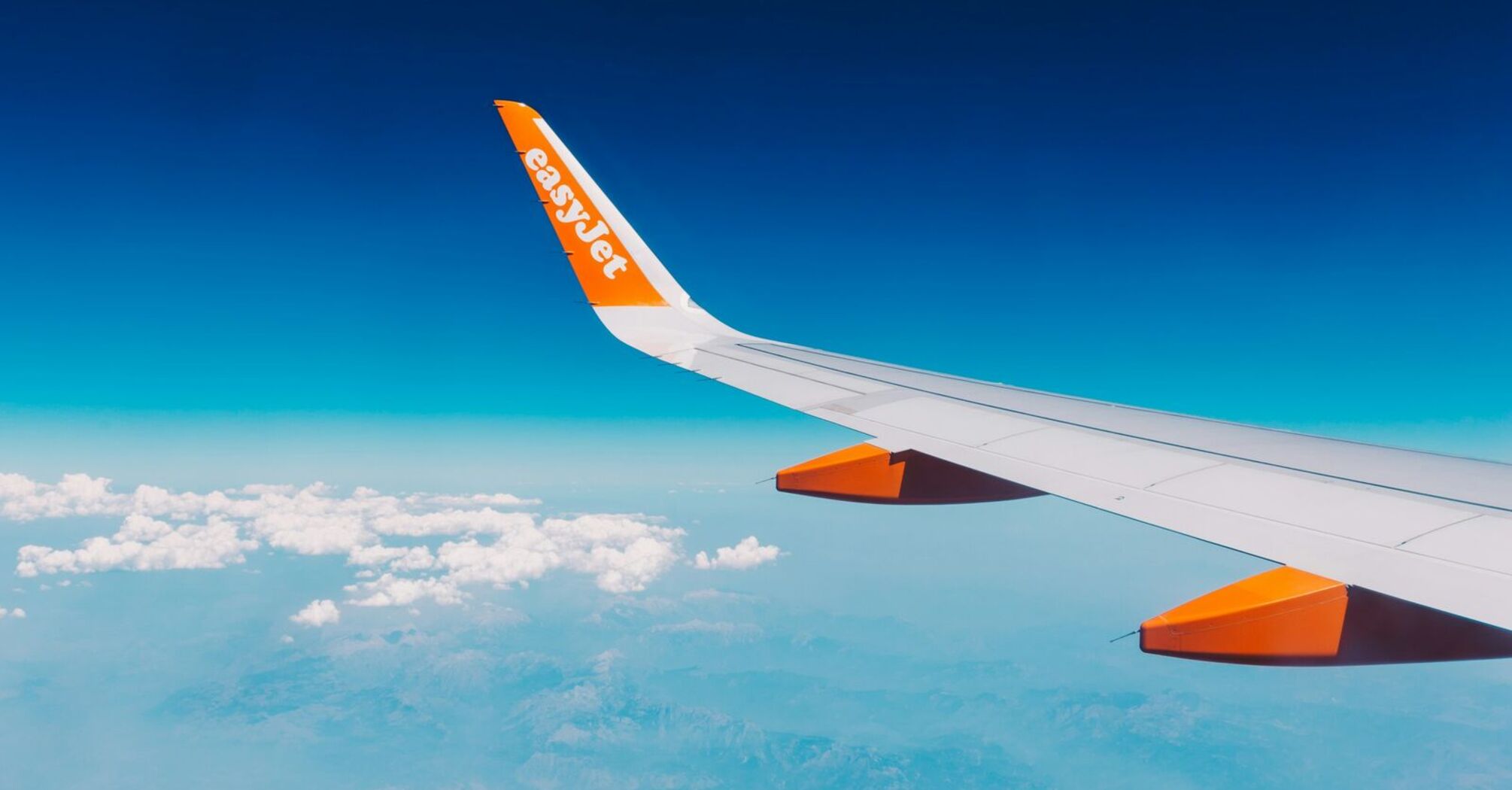 easyJet airplane wing flying above clouds and coastline
