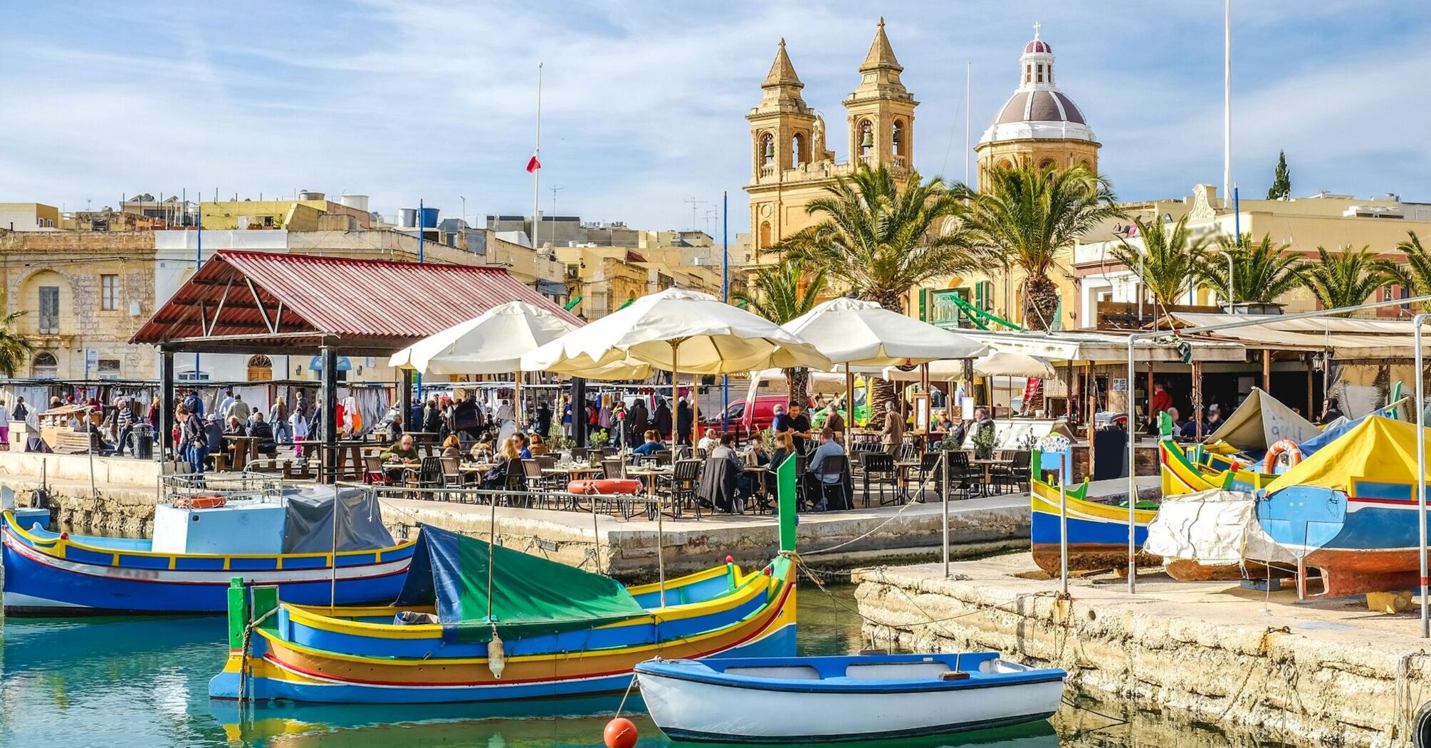 Vibrant waterfront scene in Malta with colorful boats and outdoor cafes
