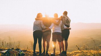 four person hands wrap around shoulders while looking at sunset