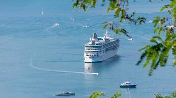 A large cruise ship sails through calm waters, surrounded by small yachts and boats