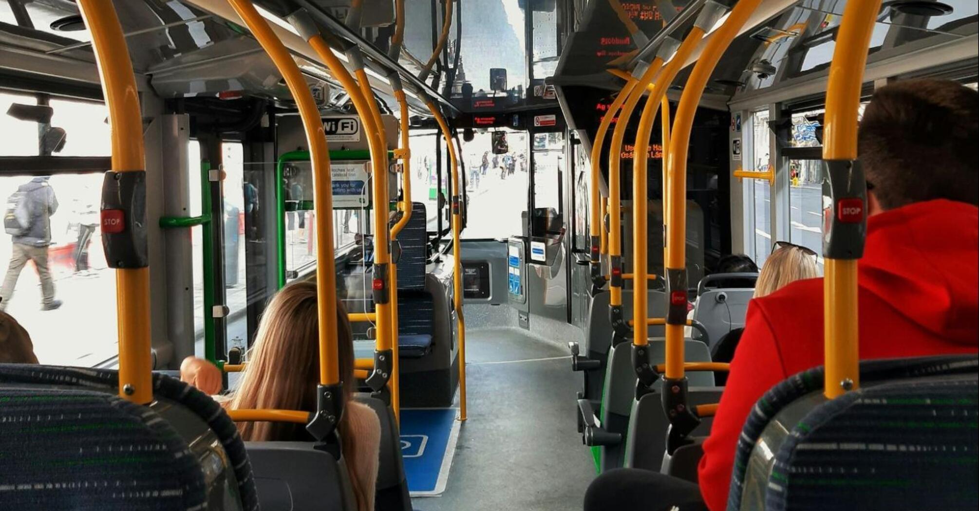 Passengers inside a modern bus with yellow handrails