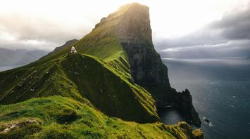 A lighthouse on a green cliff overlooking the ocean