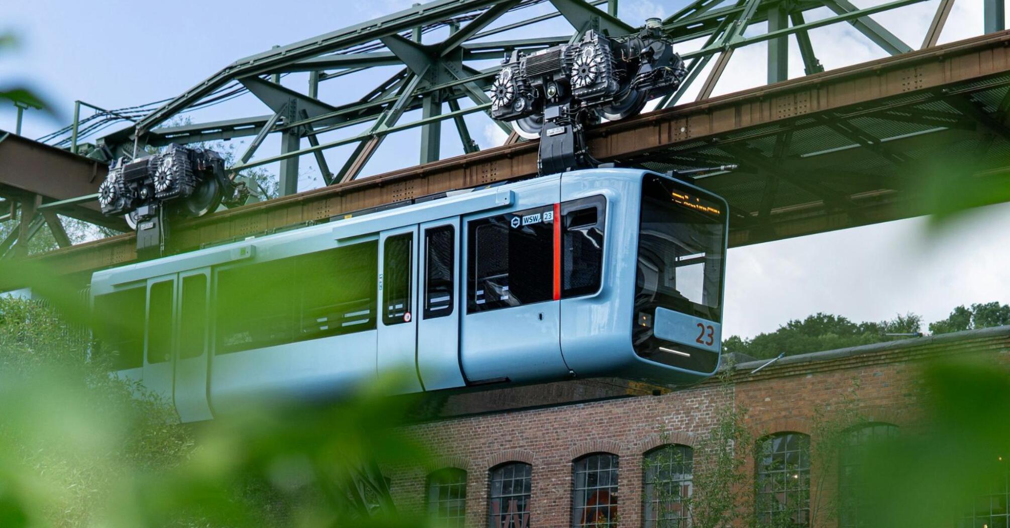 A modern blue carriage of the Schwebebahn suspension railway travels above the streets of Wuppertal, Germany