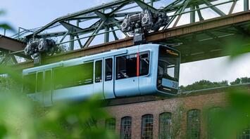 A modern blue carriage of the Schwebebahn suspension railway travels above the streets of Wuppertal, Germany