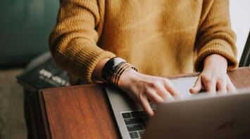 Person using a laptop, wearing a yellow sweater and bracelets