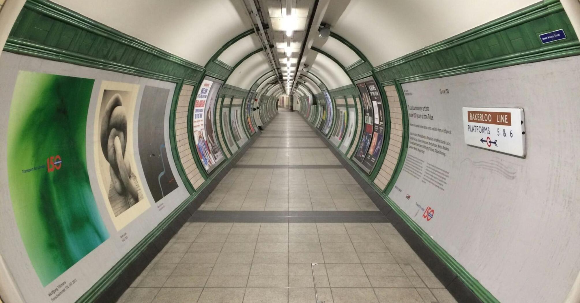 A deserted underground tunnel with green and white tiled walls, showing signs directing to the Bakerloo Line platforms