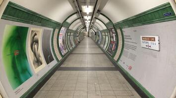A deserted underground tunnel with green and white tiled walls, showing signs directing to the Bakerloo Line platforms
