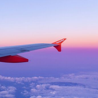 Wing of an easyJet airplane against a colorful sunset sky