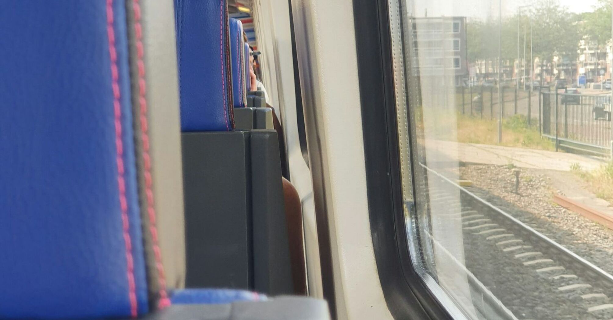 Interior view of a train with blue seats and a large window looking out onto the railway tracks