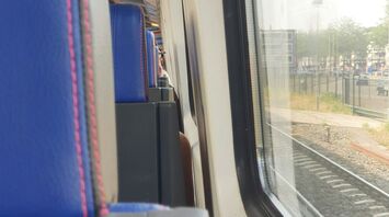 Interior view of a train with blue seats and a large window looking out onto the railway tracks