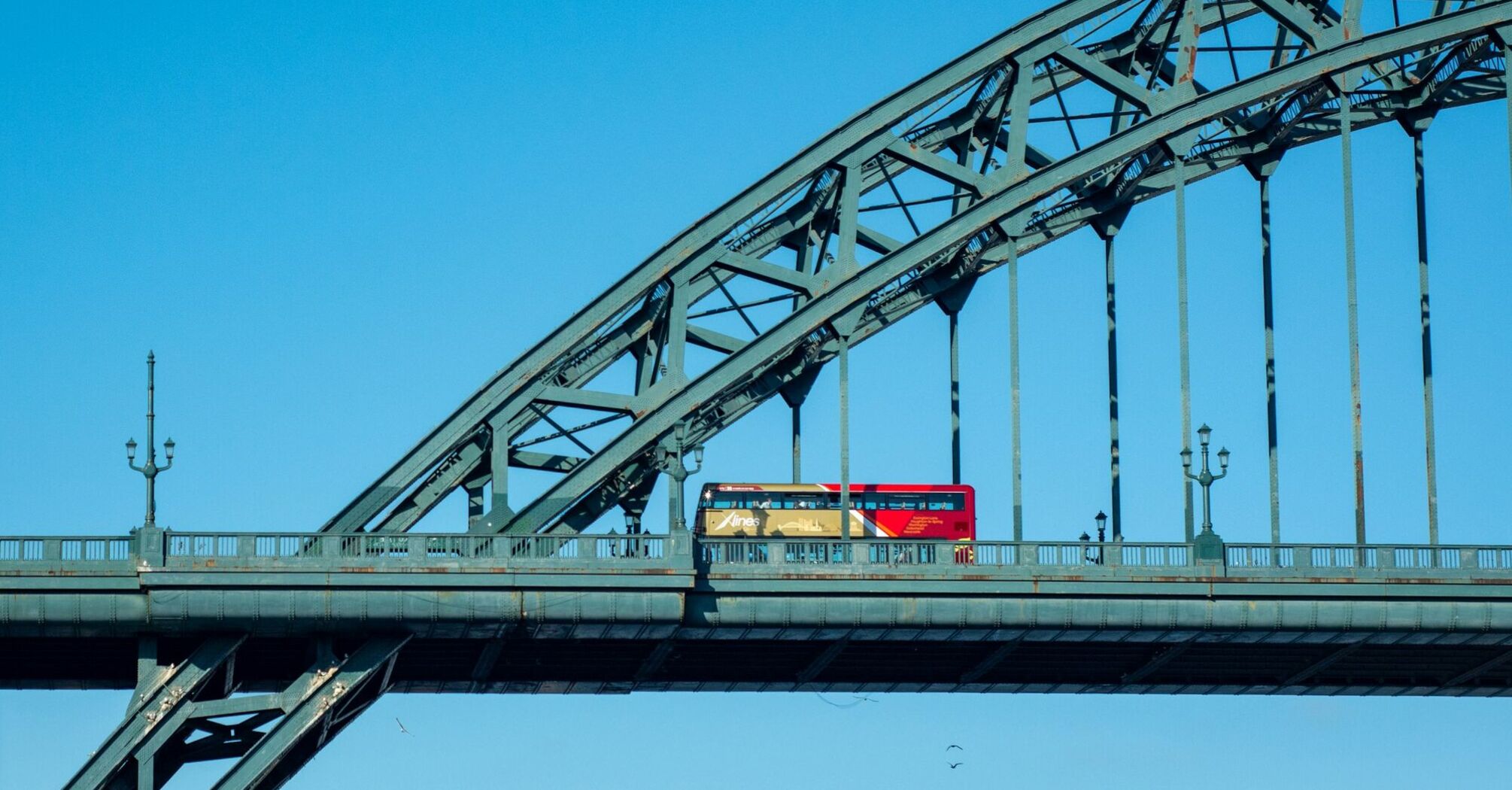 A Go North East double-decker bus crossing a steel bridge under a clear blue sky