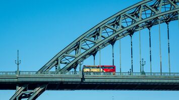 A Go North East double-decker bus crossing a steel bridge under a clear blue sky