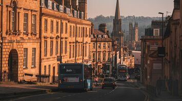 View of a historic street in the South West, showing buses, cars, and old buildings with a church in the background